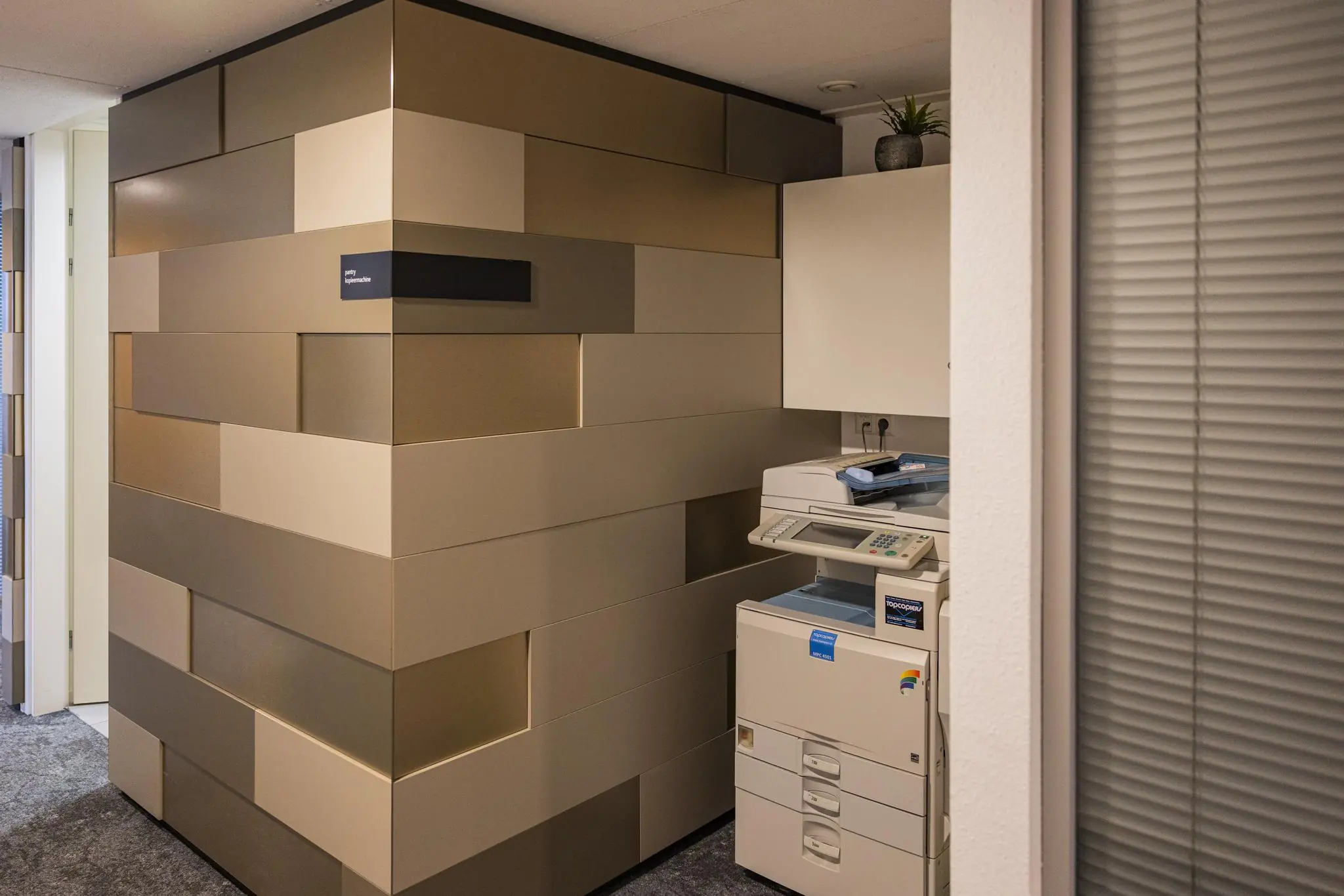 Kopieerruimte met een printer naast een modern betegelde muur in kantoorgebouw Middenburcht.