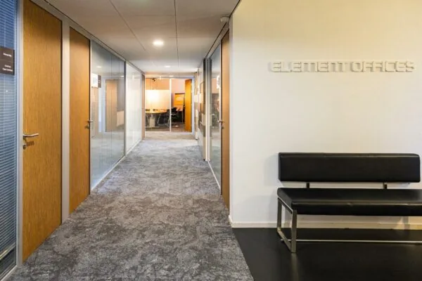 Gang in het kantoorgebouw Element Offices met glazen wanden, houten deuren en een zwarte wachtbank.