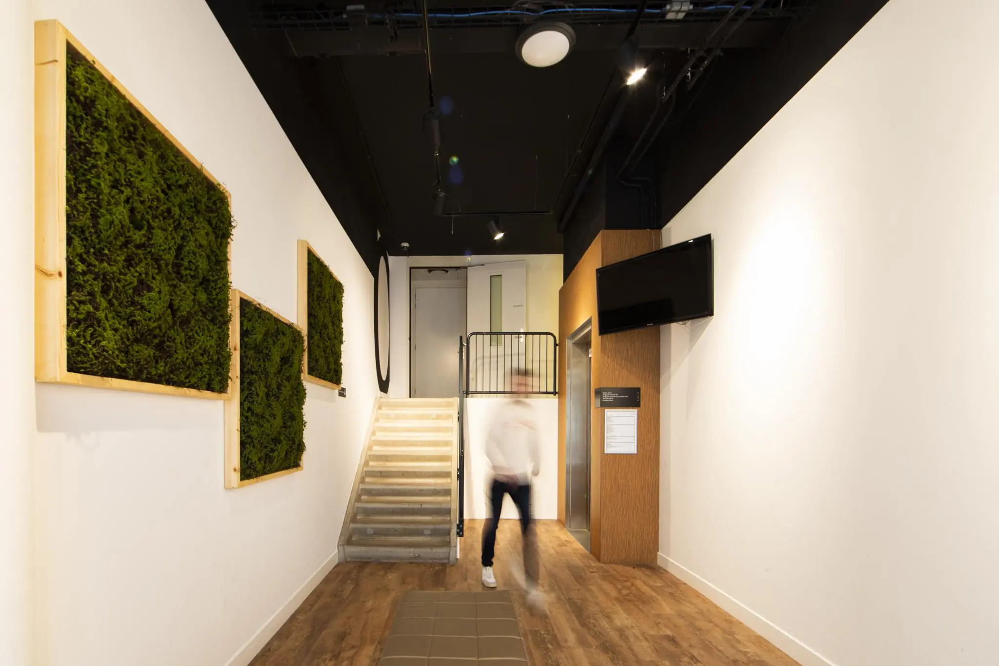 Moderne entreehal van Middenburcht met trap, lift, muurdecoratie van mos en een plafond met zwarte afwerking.
