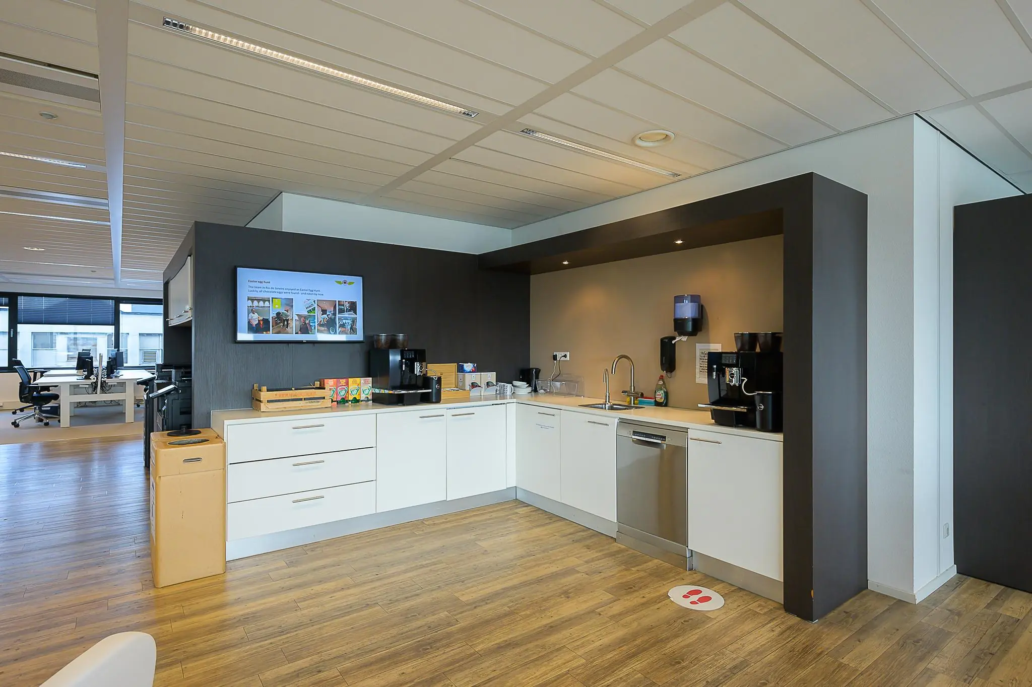 Moderne kantoorkeuken aan de Willingestraat met koffiezetapparaten, vaatwasser en een zithoek op de achtergrond.