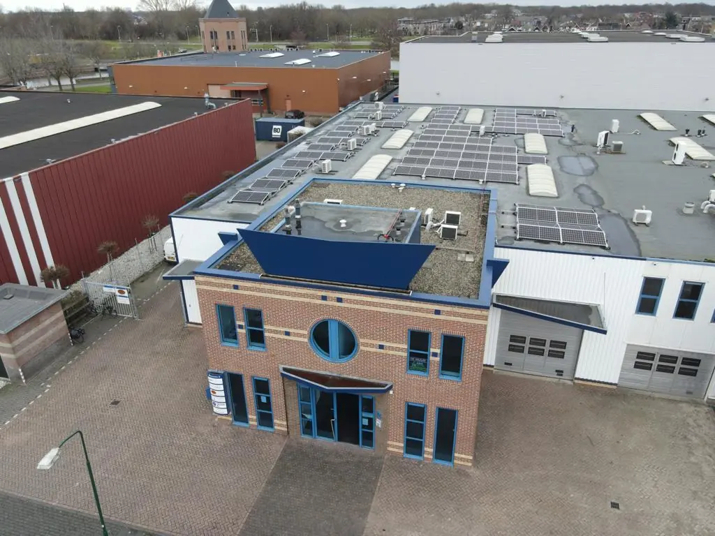 Luchtfoto van het bedrijfsgebouw Bergveste met zonnepanelen op het dak en een bakstenen voorgevel met blauwe accenten.