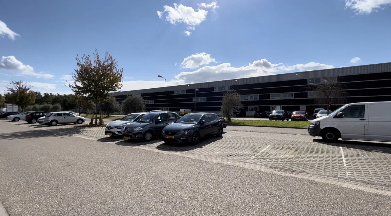 Parkeerplaats met auto's voor een modern zwart bedrijfspand aan de Bergveste op een zonnige dag.