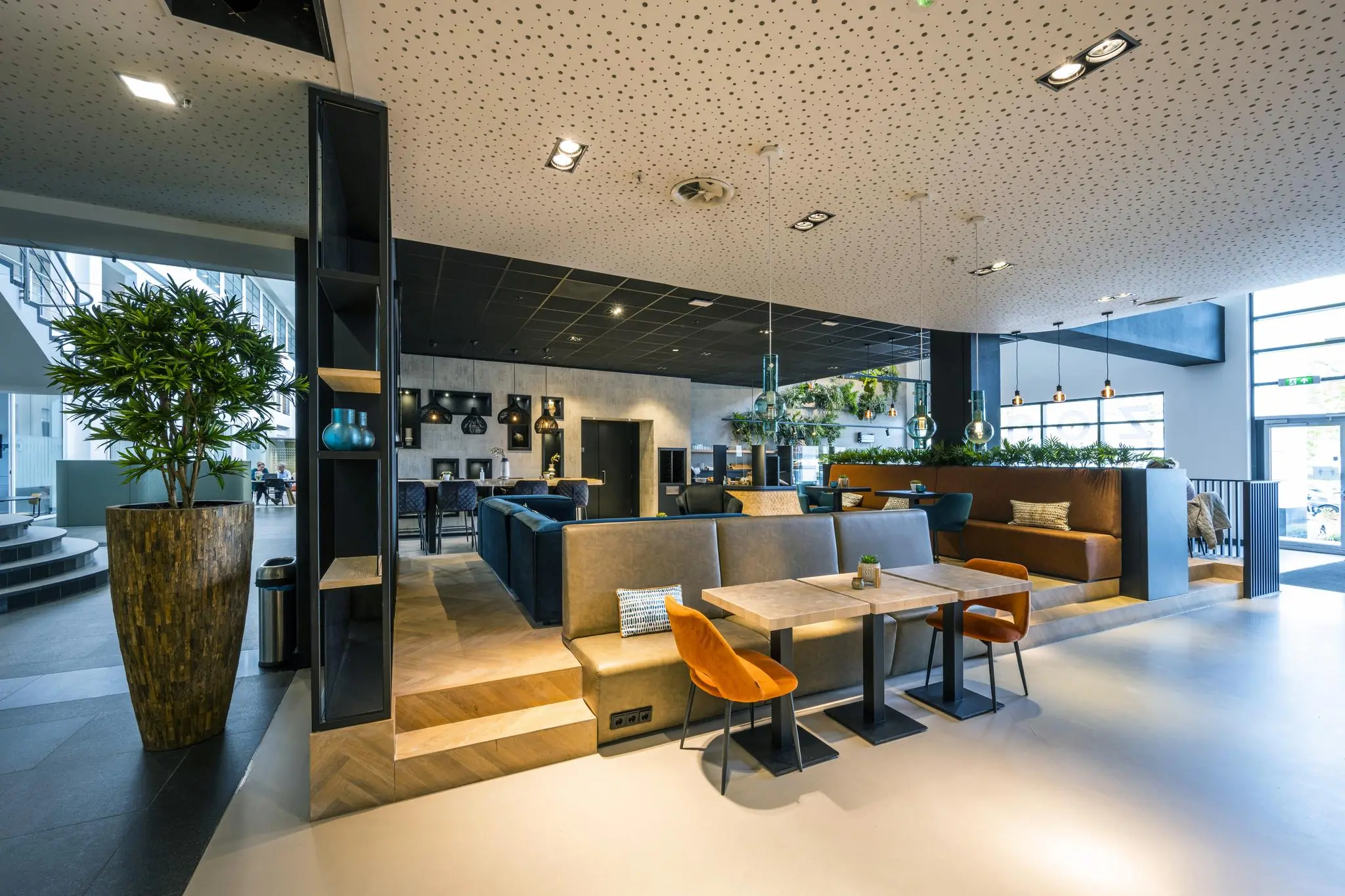 Moderne en sfeervolle lounge- en werkruimte aan de Laarderhoogtweg met zitbanken, tafels en hanglampen.