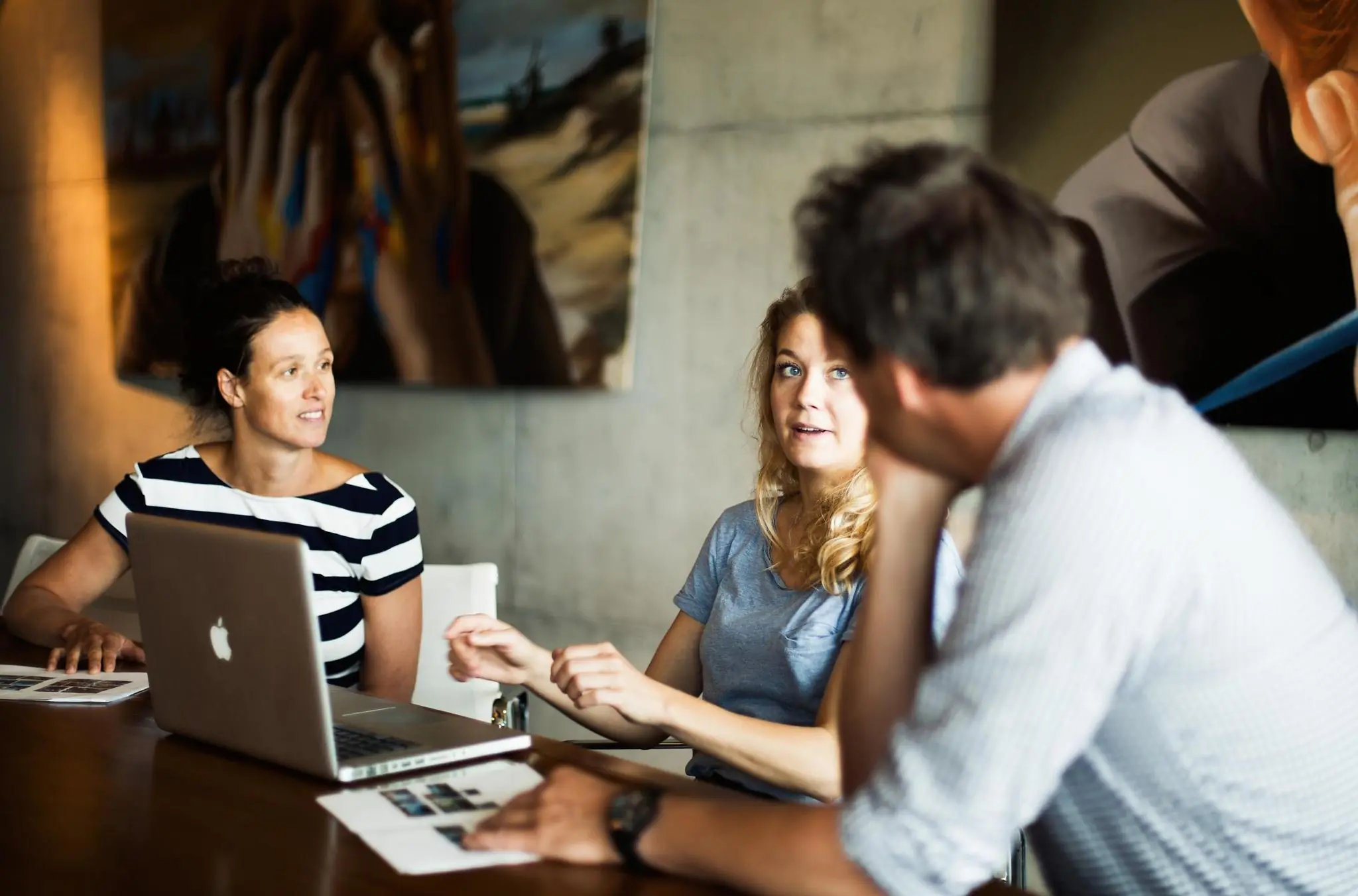 Drie mensen in gesprek tijdens een vergadering aan een tafel met een laptop en papieren, in een modern kantoor aan de Orteliuslaan.