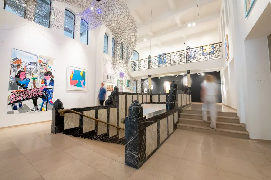 Licht en modern interieur van een kunstgalerie aan het Weesperplein met kleurrijke schilderijen en een marmeren trap.