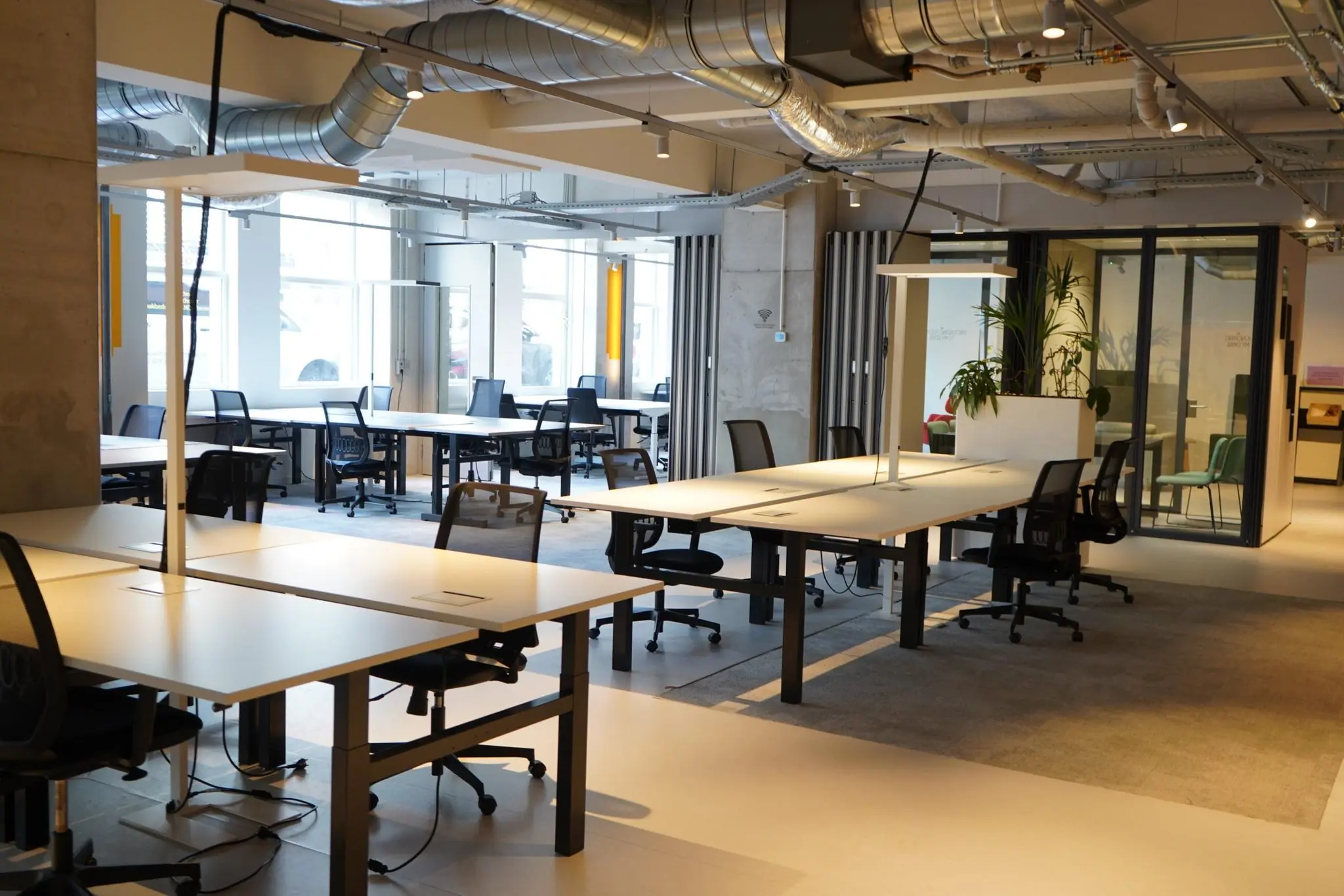 Moderne open kantoorruimte op het Weesperplein met bureaus, bureaustoelen en glazen vergaderruimte.