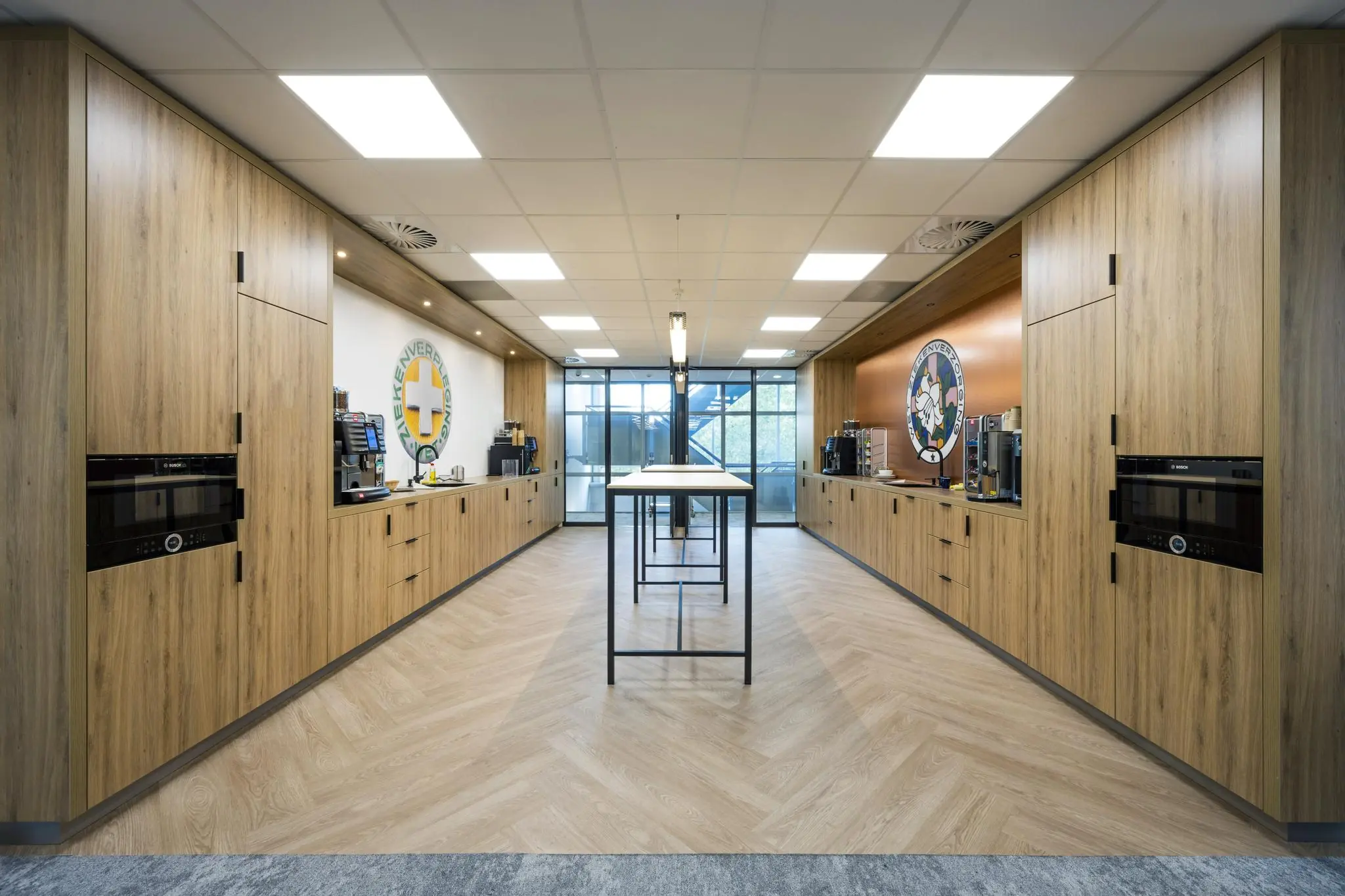 Moderne bedrijfskeuken aan de Orteliuslaan met houten kasten, koffieapparaten en zitruimte met hoge tafels.