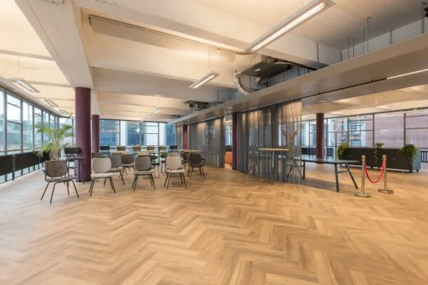 Moderne en ruime evenementen- of vergaderruimte aan de Vlasmarkt met houten visgraatvloer, diverse stoelen en glazen wanden met gordijnen.