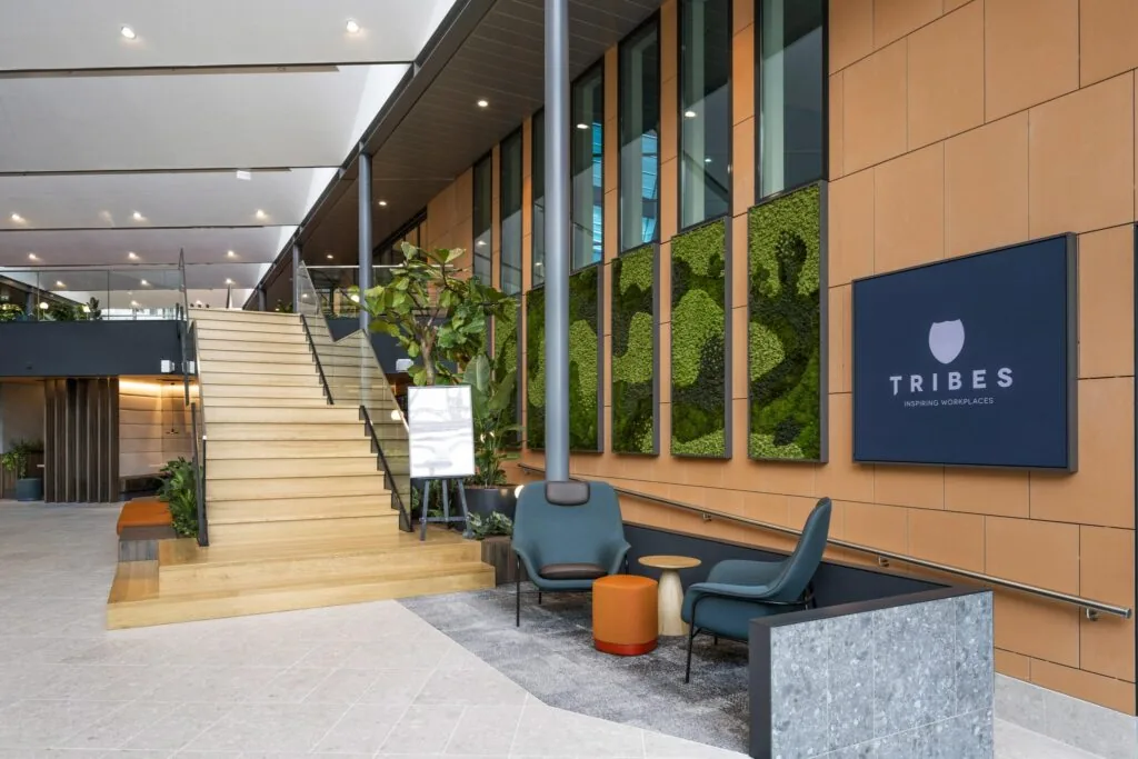 Moderne kantoorlobby aan de Jachthavenweg met houten trap, groene plantenwand en Tribes-logo.