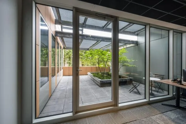 Doorkijk vanuit een kantoorruimte naar een groene binnentuin met zitgelegenheid aan de Jachthavenweg.