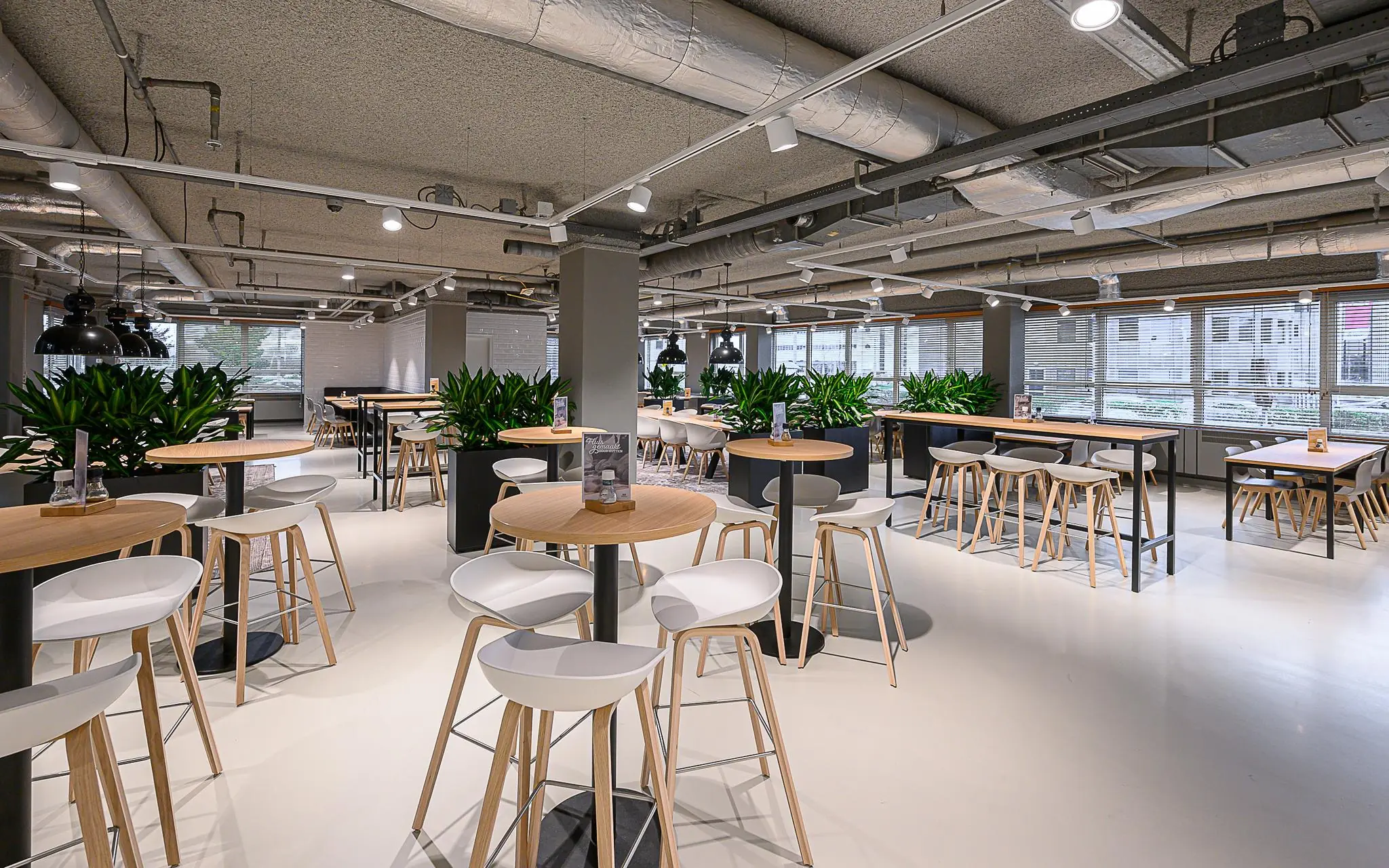 Modern ingerichte bedrijfsrestaurant aan de Rivium 1e Straat met hoge tafels, barkrukken en veel groen.