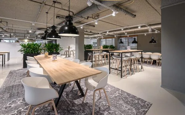 Modern ingerichte kantine aan de Rivium 1e Straat met houten tafels, witte stoelen en hanglampen.