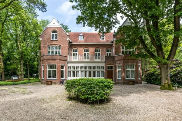 Statige, vrijstaande villa aan de Amersfoortsestraat, omringd door bomen en grindtuin.