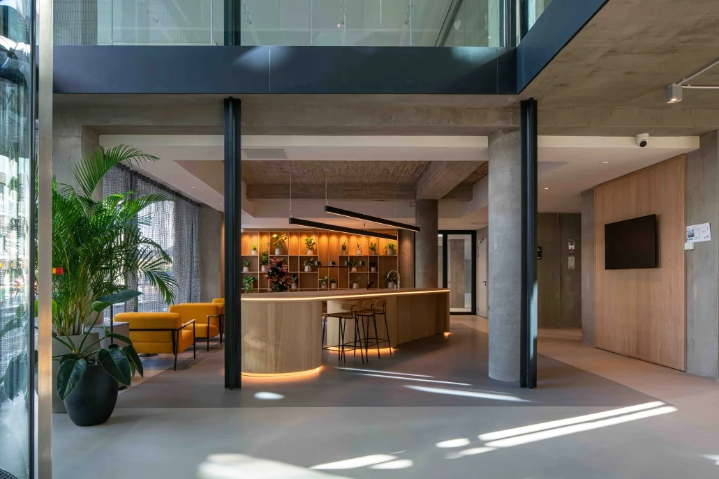 Moderne lobby met houten receptiebalie, plantenwand en gele stoelen aan de Catharijnesingel.