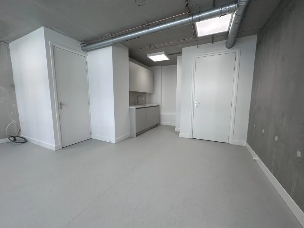 Moderne, lege studio aan de Willem Parelstraat met witte deuren, een kleine keuken en zichtbare ventilatiebuizen aan het plafond.