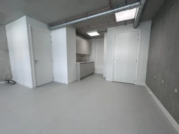 Moderne, lege studio aan de Willem Parelstraat met witte deuren, een kleine keuken en zichtbare ventilatiebuizen aan het plafond.