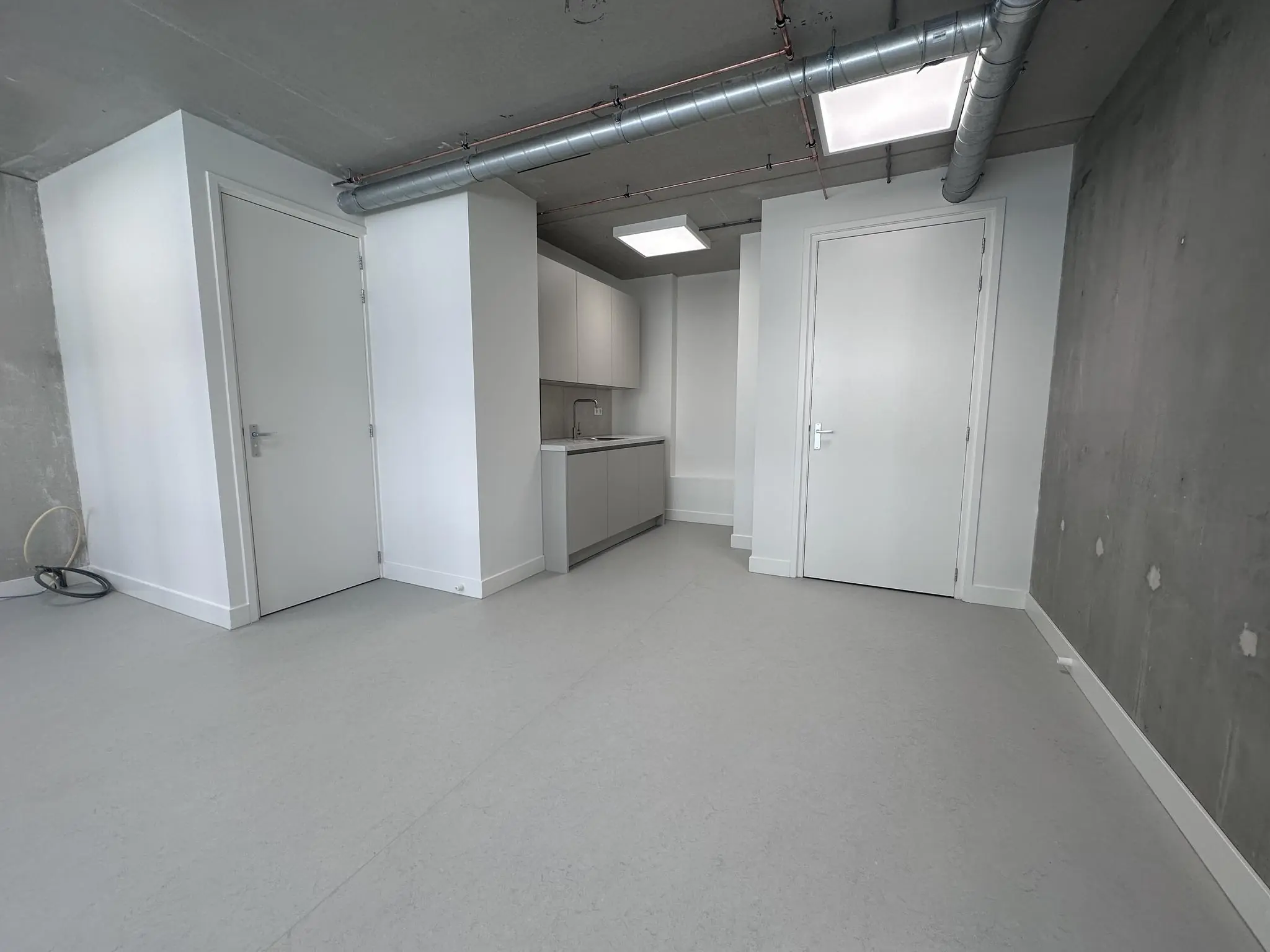 Moderne, lege studio aan de Willem Parelstraat met witte deuren, een kleine keuken en zichtbare ventilatiebuizen aan het plafond.