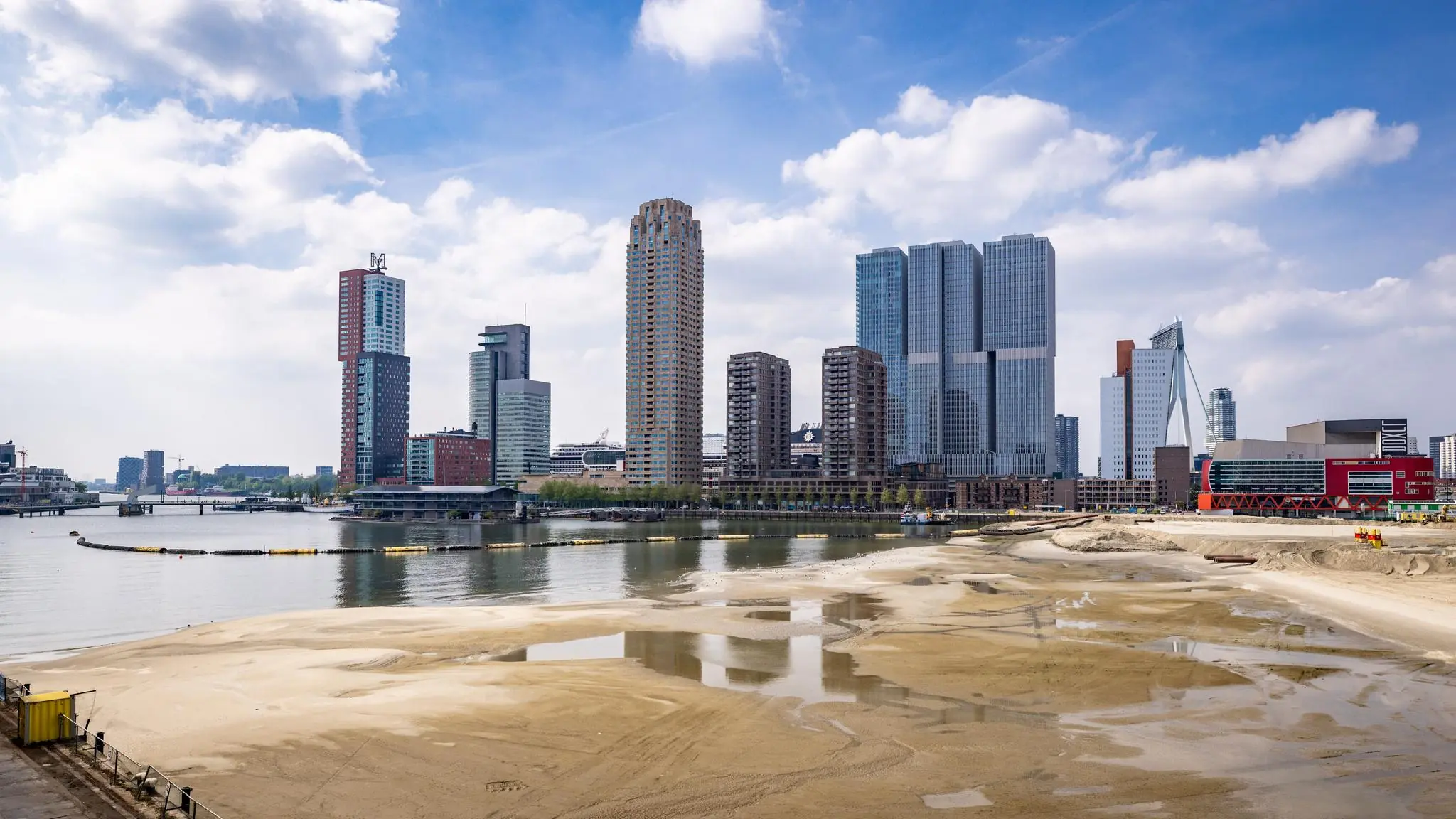 Skyline van Rotterdam met zicht op de Rijnhavenkade, hoogbouw en het zandige bouwterrein op de voorgrond.