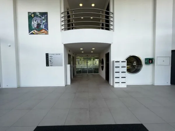 Ingang van een modern kantoorgebouw met brievenbussen, een schilderij aan de muur en een overzichtsbord van bedrijven aan de Nevelgaarde.