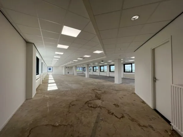 Lege kantoorruimte in Nevelgaarde met systeemplafond, grote ramen en onafgewerkte vloer.
