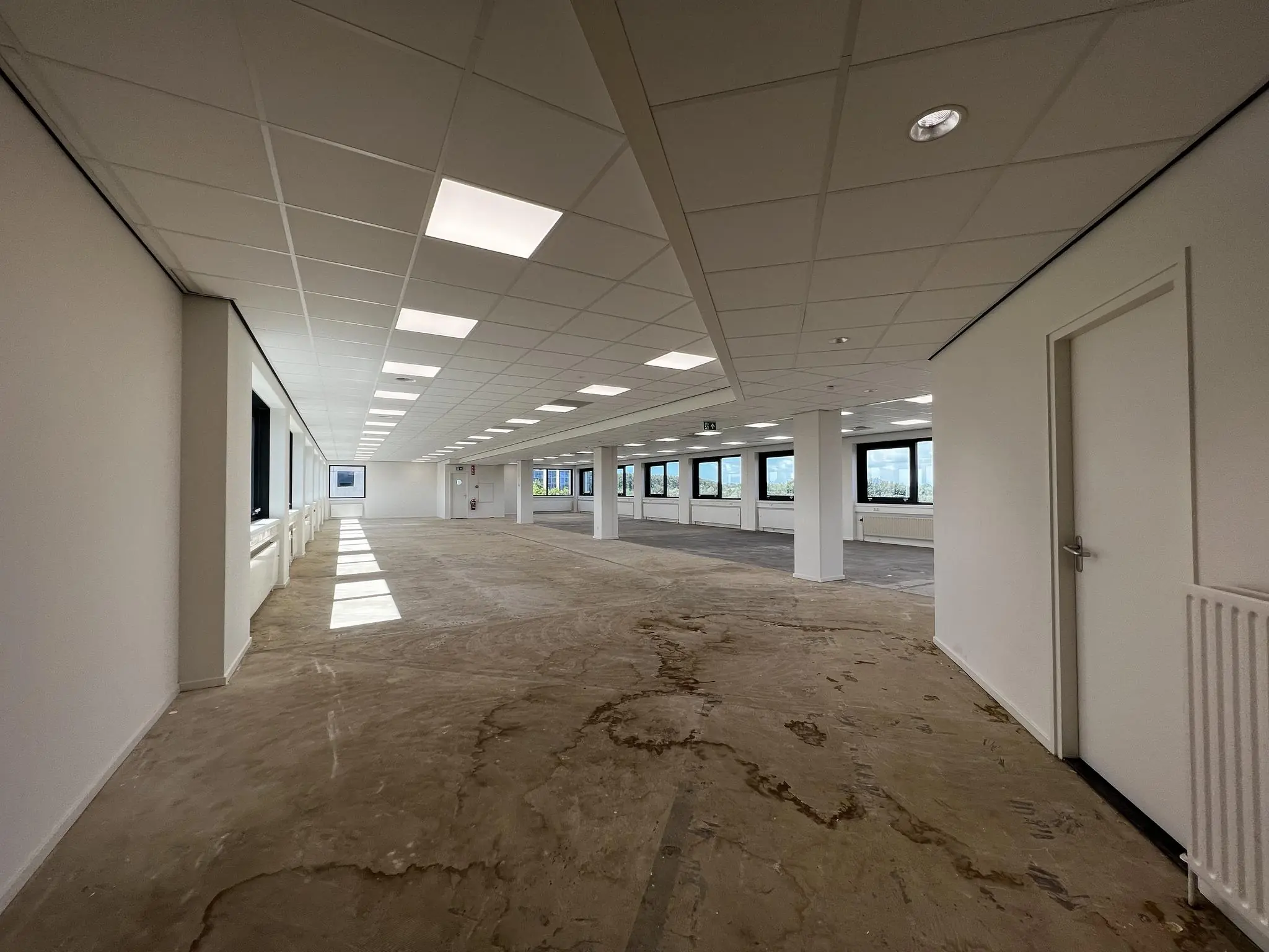 Lege kantoorruimte in Nevelgaarde met systeemplafond, grote ramen en onafgewerkte vloer.