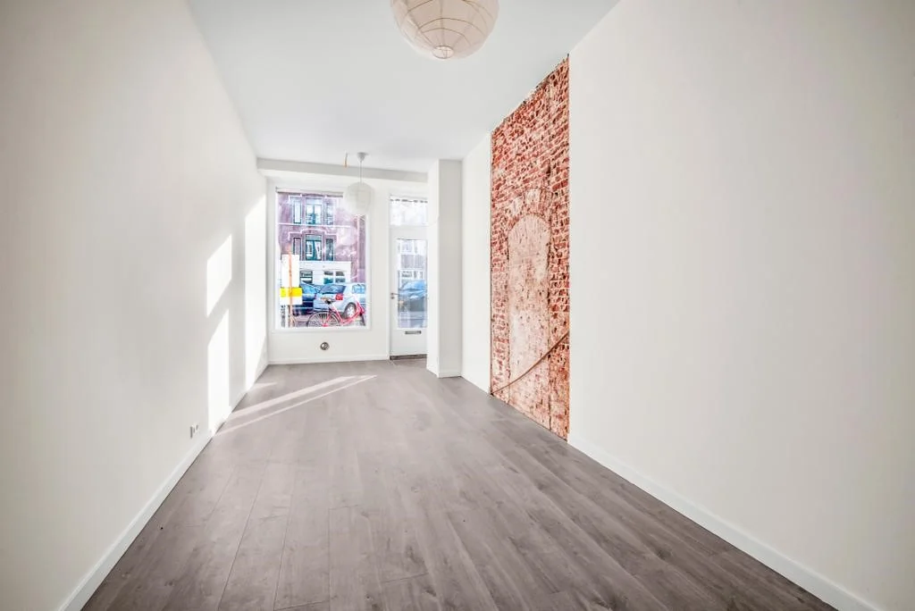 Lichte, smalle woonkamer aan de Westerstraat met houten vloer en opvallende bakstenen muurprint.