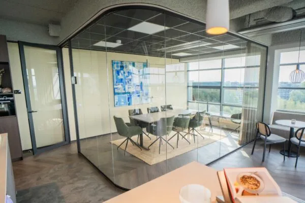 Moderne vergaderruimte met glazen wanden aan de Joop Geesinkweg, ingericht met groene stoelen, een houten tafel en een blauw kunstwerk aan de muur.