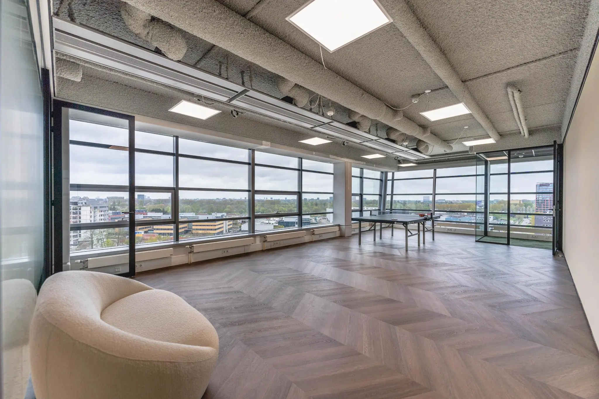 Moderne, zonnige kantoorlounge aan de Joop Geesinkweg met panoramisch uitzicht, een ronde fauteuil en een pingpongtafel.