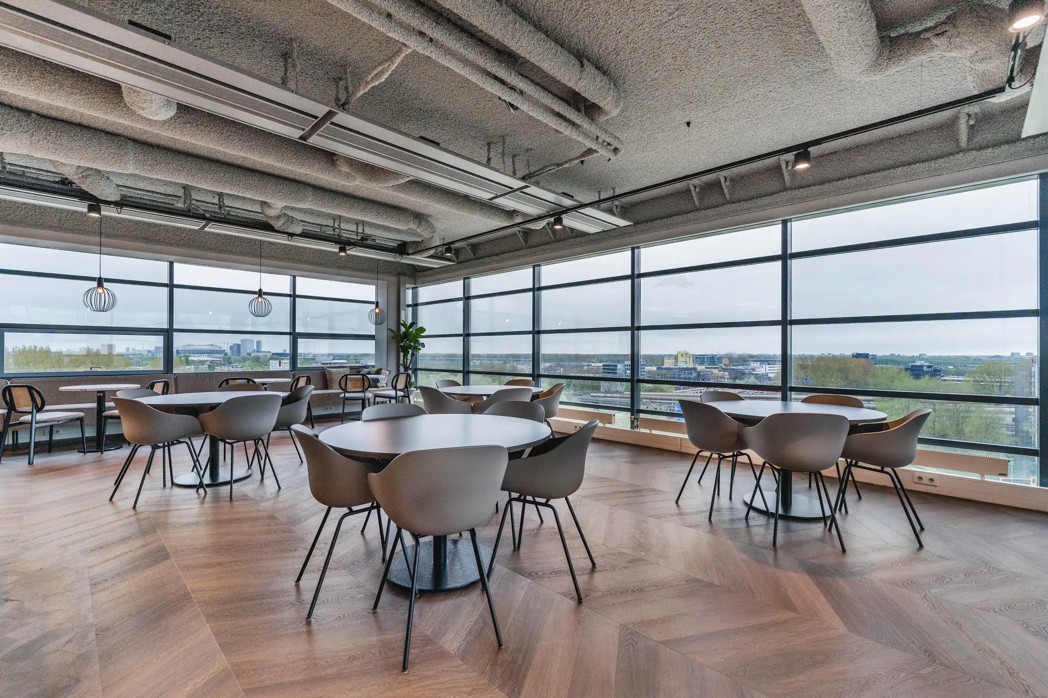 Moderne en lichte kantoorruimte aan de Joop Geesinkweg met ronde tafels, designstoelen en panoramisch uitzicht over de stad.