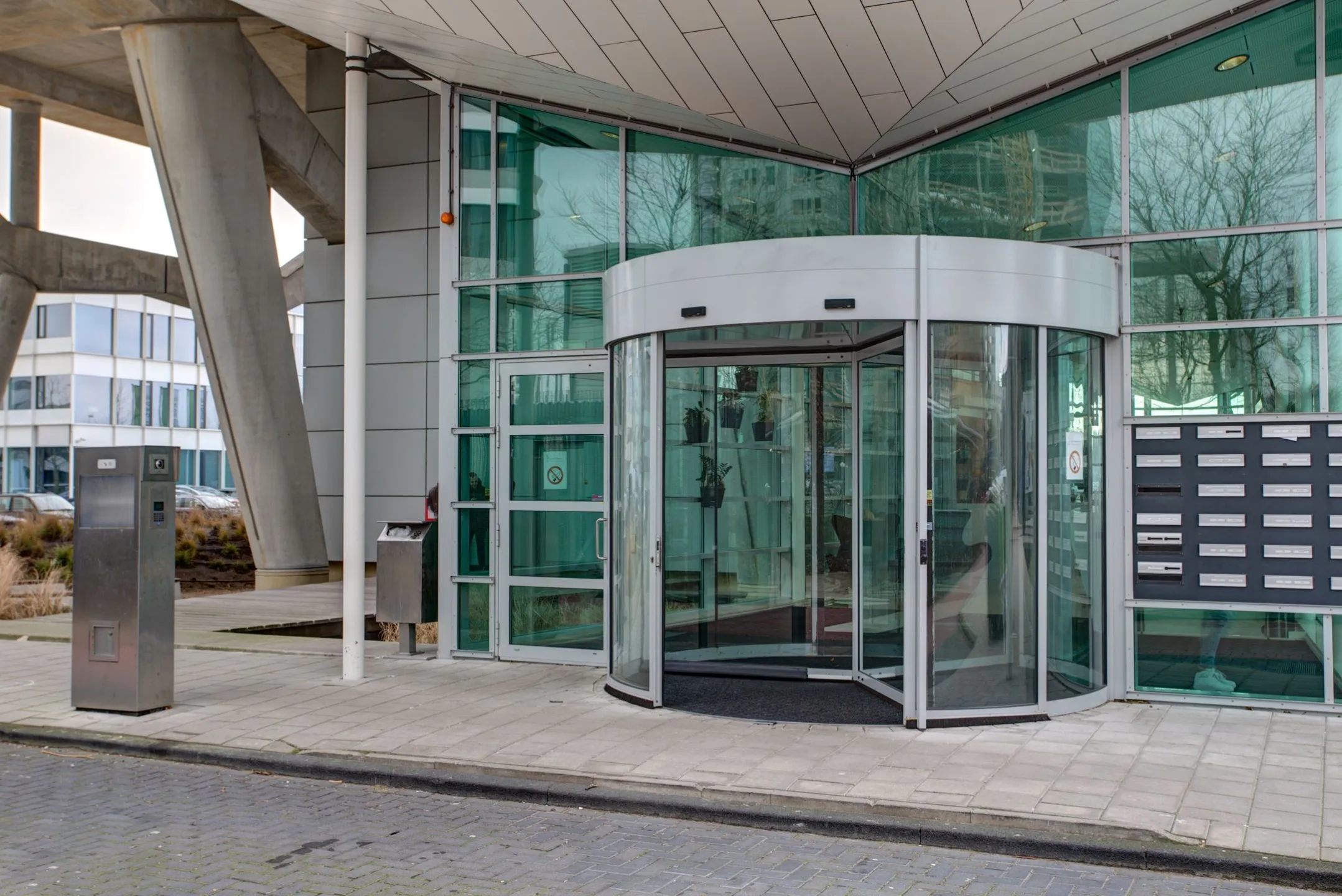 Een glazen draaideur bij de ingang van een modern kantoorgebouw met brievenbussen aan de zijkant.