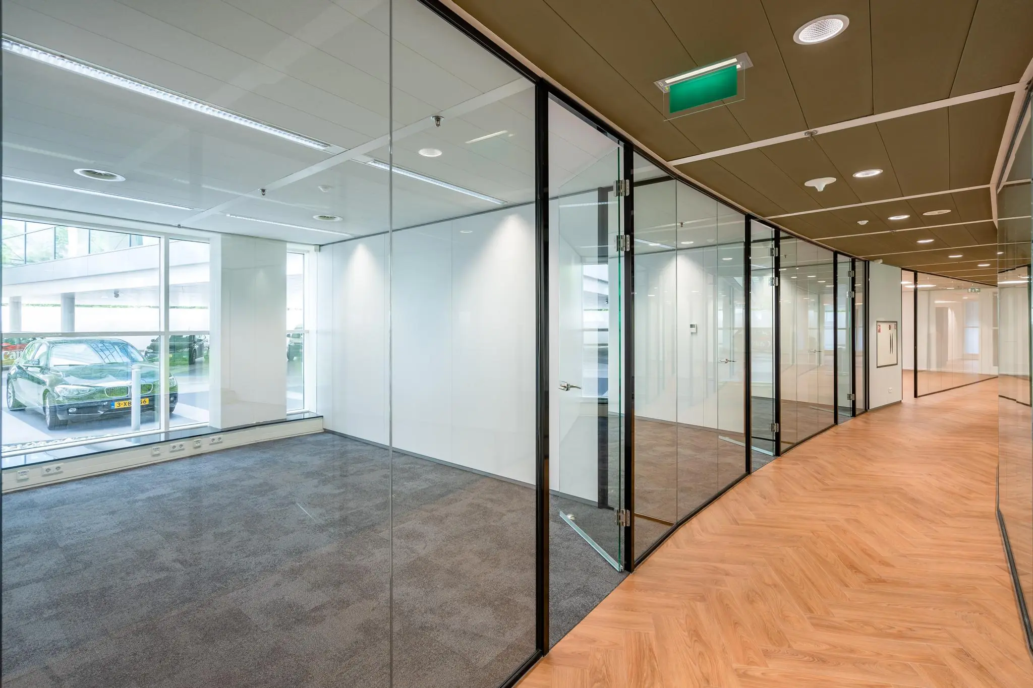 Moderne kantoorruimte aan de Newtonlaan met glazen wanden, houtlook vloer en uitzicht op een parkeerplaats.