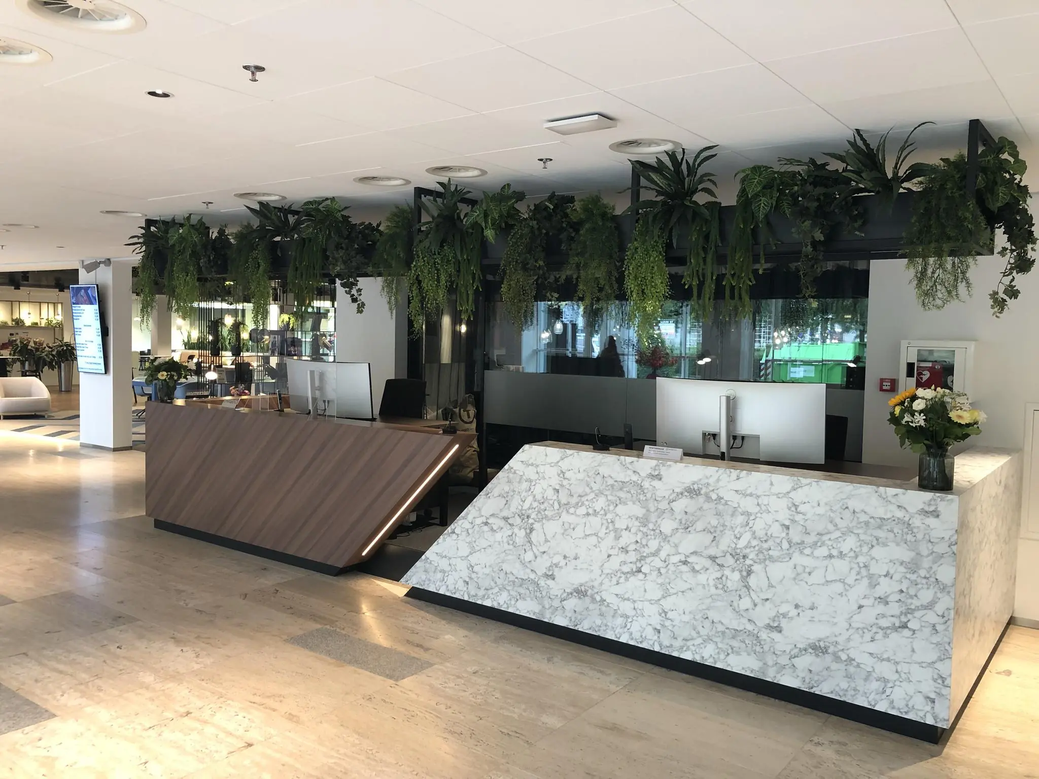 Moderne receptiebalie op Newtonlaan met marmeren en houten afwerking, omgeven door hangende groene planten.