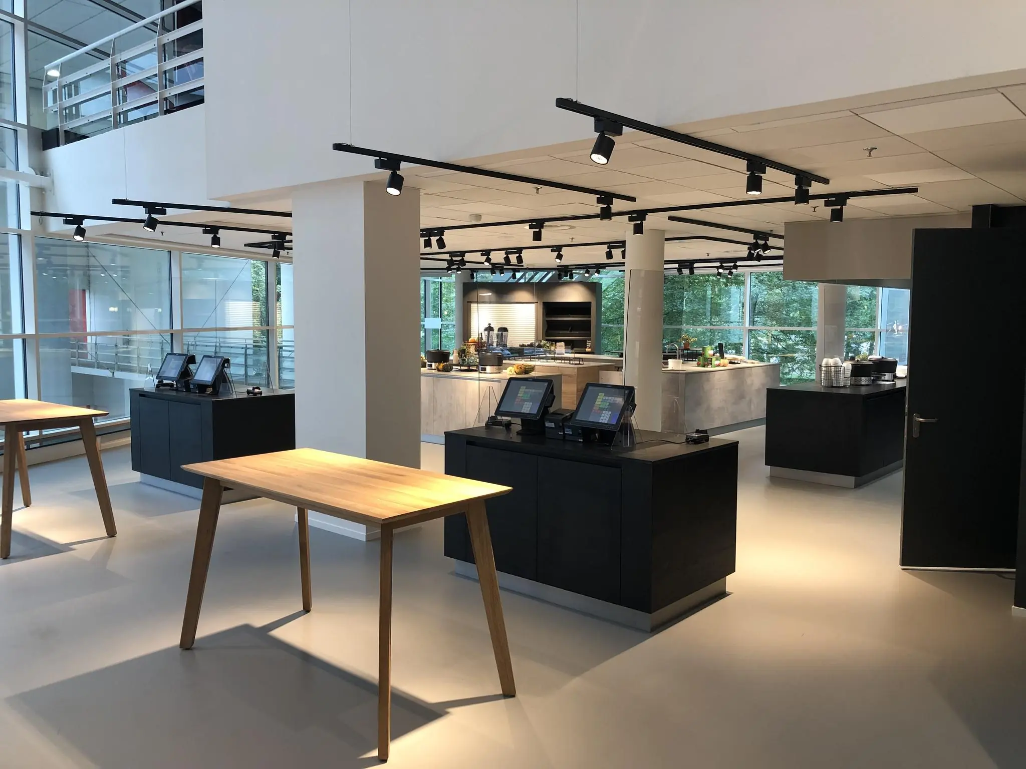 Moderne, lichte bedrijfskantine aan de Newtonlaan met zelfbedieningsstations en houten tafels.