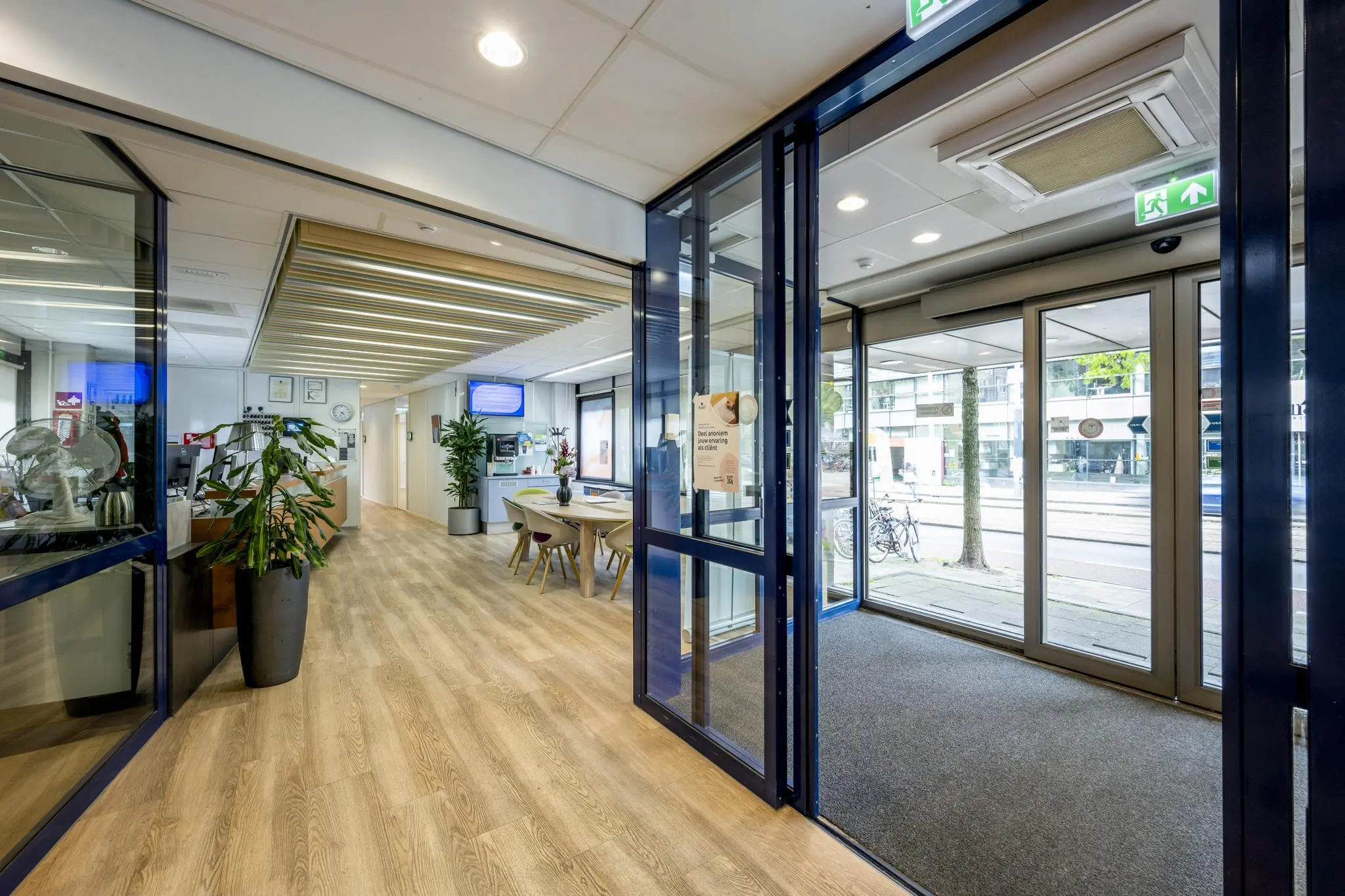 Ingang en ontvangstruimte van een modern kantoorpand aan de Sarphatistraat met houten vloer, glazen deuren en wachtruimte.