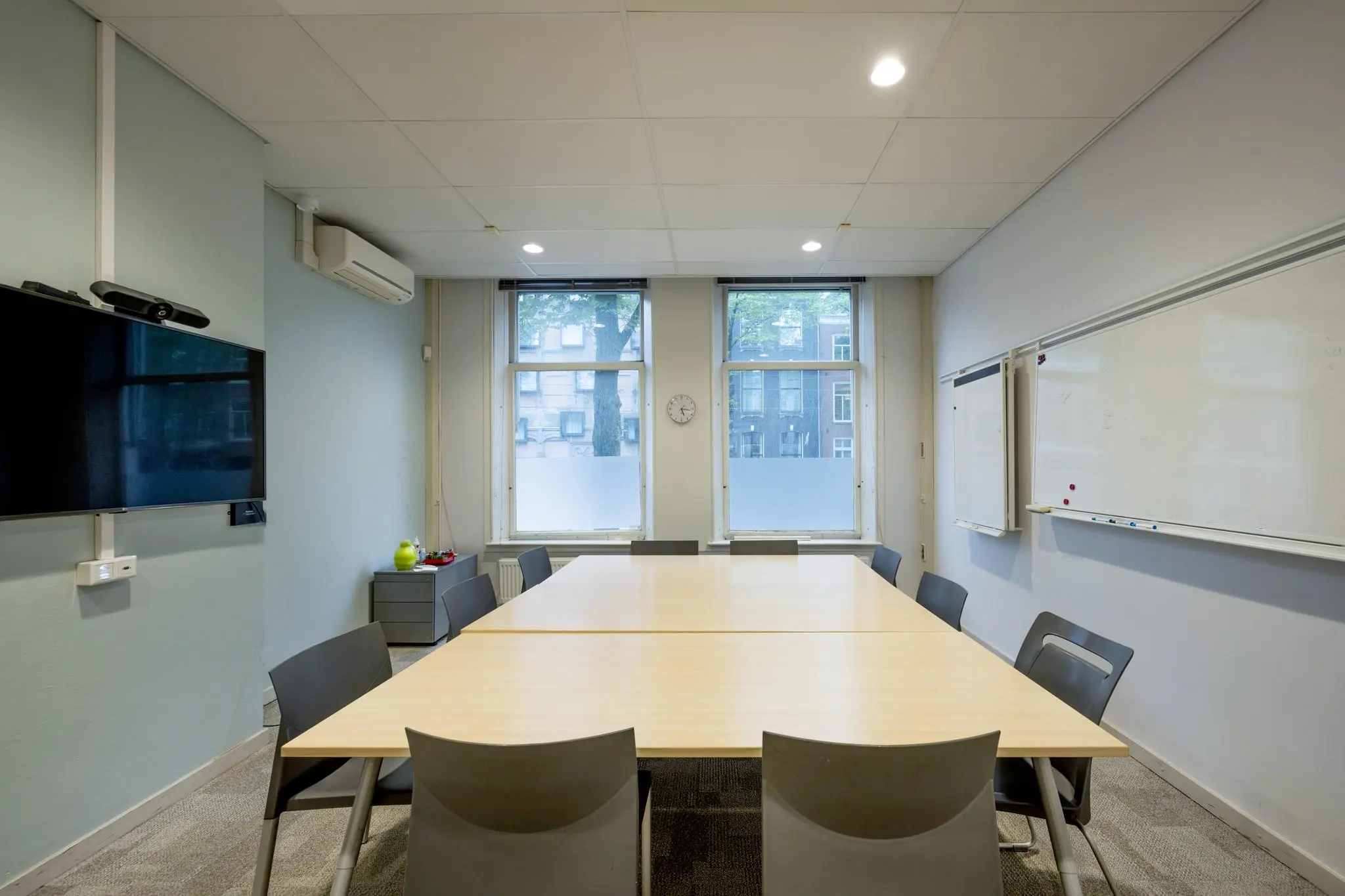 Vergaderruimte aan de Sarphatistraat met een grote tafel, stoelen, whiteboard en een flatscreen aan de muur.