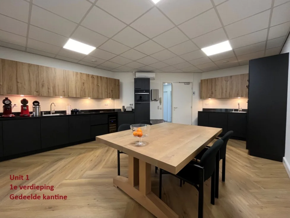 Moderne gedeelde kantine op de eerste verdieping van Unit 1 met houten vloer, ruime keuken en vergadertafel.