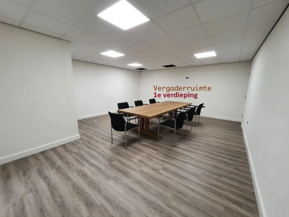Vergaderruimte op de eerste verdieping met een grote houten tafel en zwarte stoelen in een modern interieur.