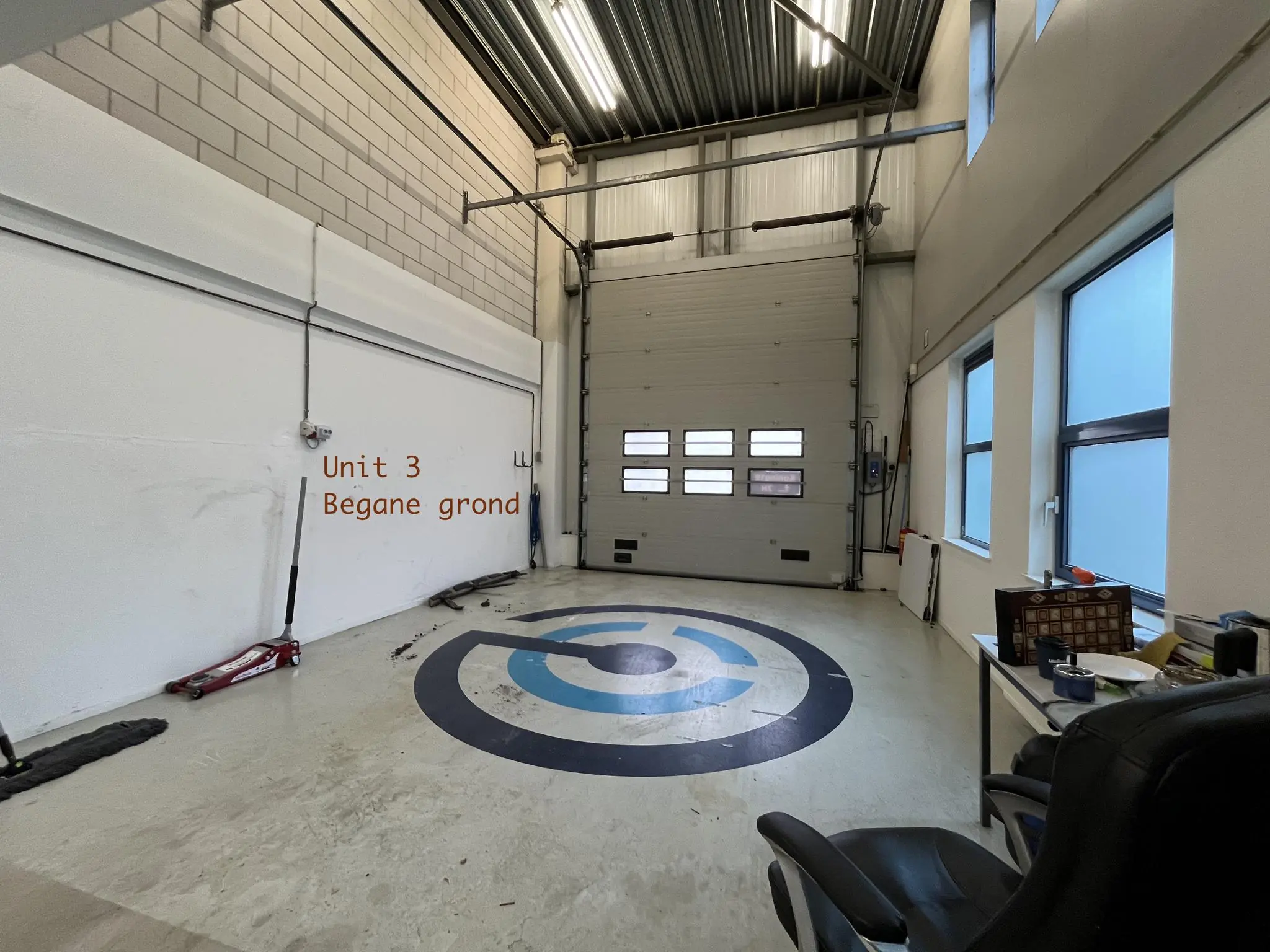 Interieur van werkruimte Unit 3 op de begane grond met industriële garagedeur en bedrijfslogo op de vloer.