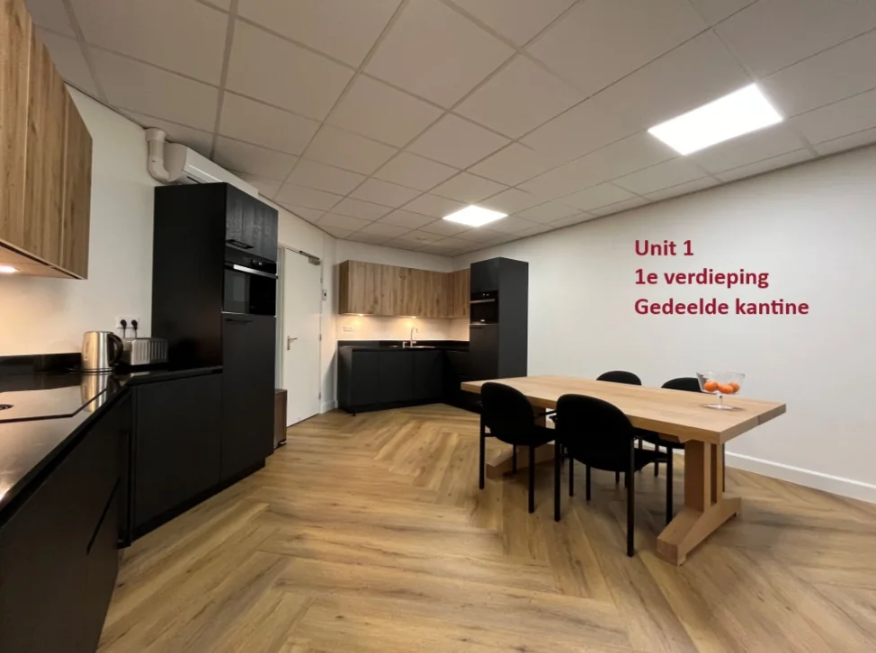 Moderne gedeelde kantine op de eerste verdieping van Unit 1 met zwarte keukenkasten, houten accenten en een houten eettafel met vier stoelen.