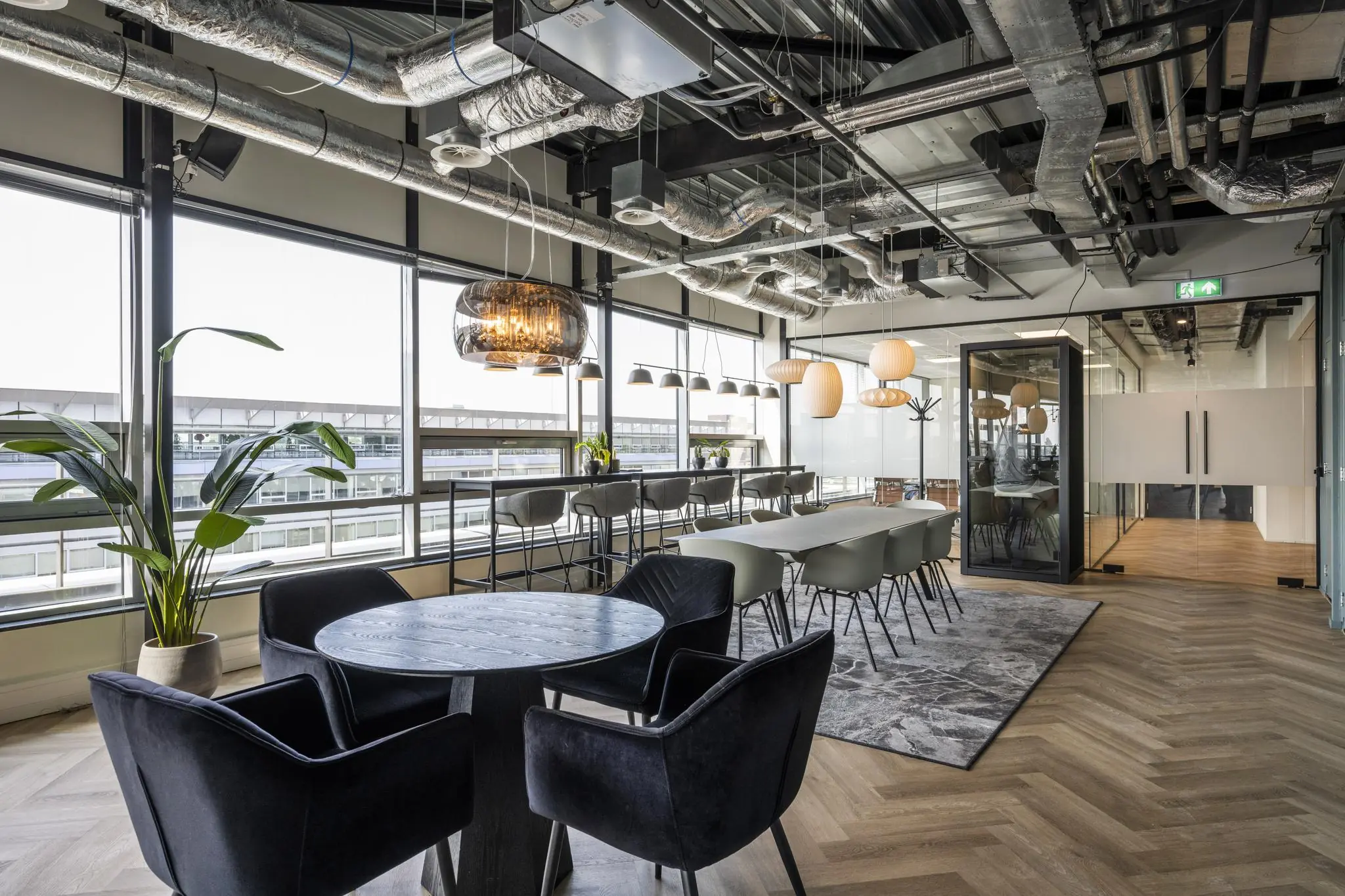 Moderne kantoorlounge aan het Bos en Lommerplein met zithoeken, hoge ramen en industriële plafondafwerking.