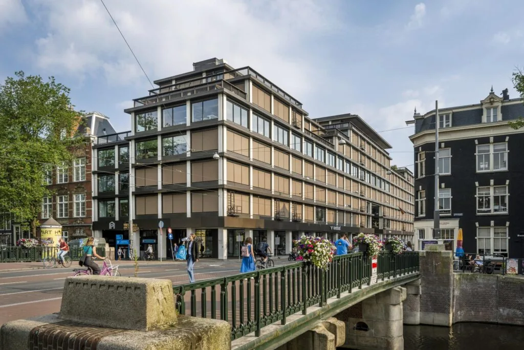 Straatbeeld van de Vijzelstraat in Amsterdam met moderne en klassieke gebouwen, zichtbaar vanaf een brug over een gracht.