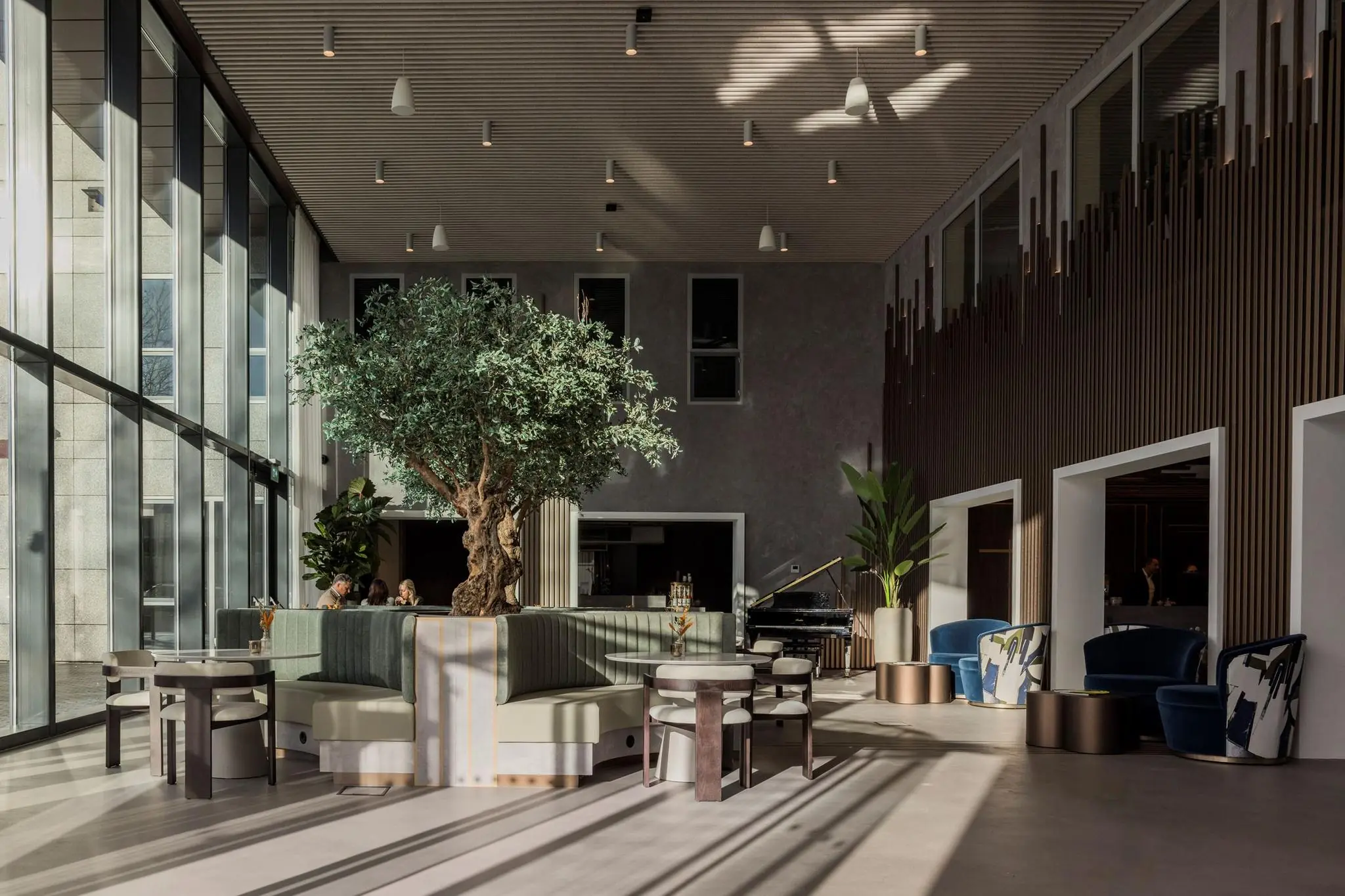 Moderne, lichte lounge met grote raampartijen, een centrale boom en stijlvolle zitplekken in het Diemerhof gebouw.