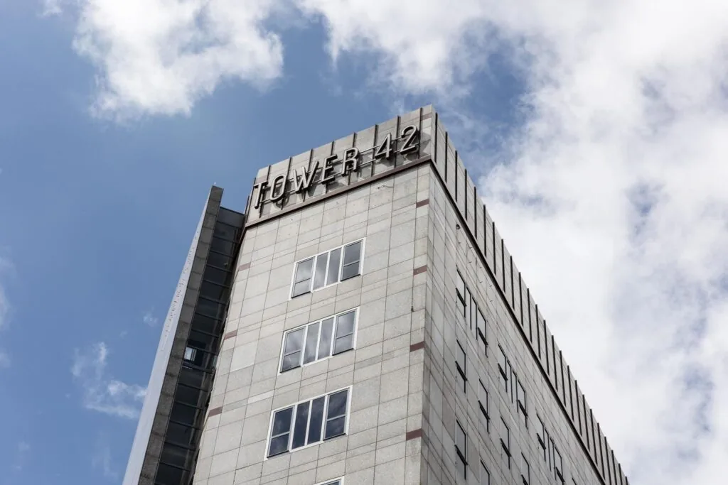 Hoekaanzicht van de bovenste verdiepingen van kantoorgebouw Tower 42 in Diemen tegen een deels bewolkte lucht.