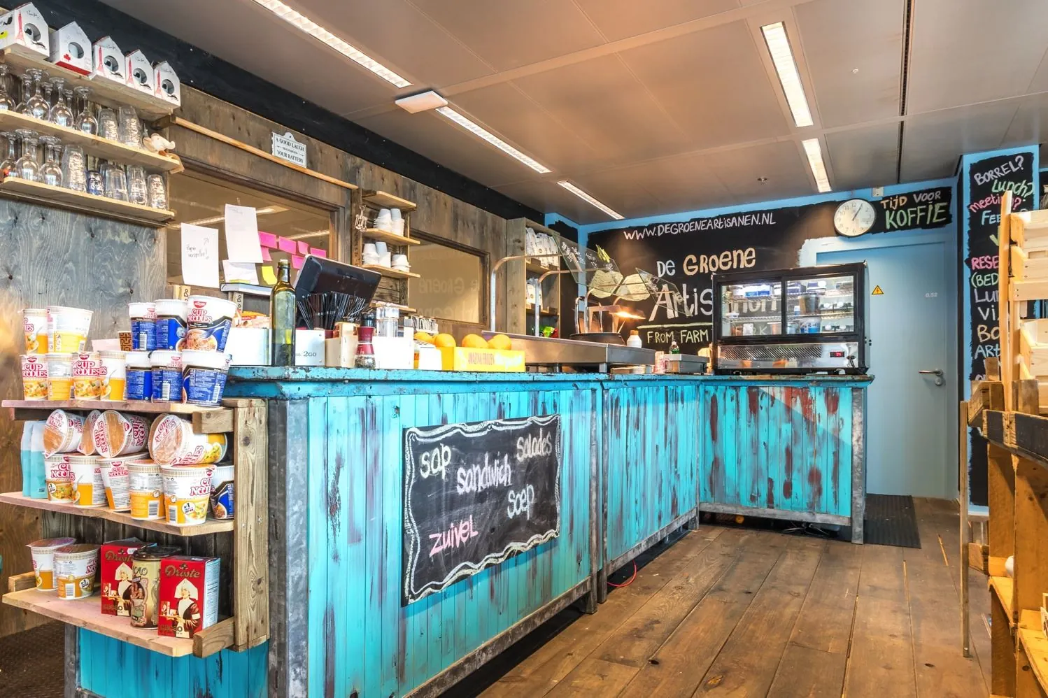 Kleurrijke eet- en koffiekraam van De Groene Artisan aan de Reactorweg met een turquoise houten balie en uitgestalde producten.