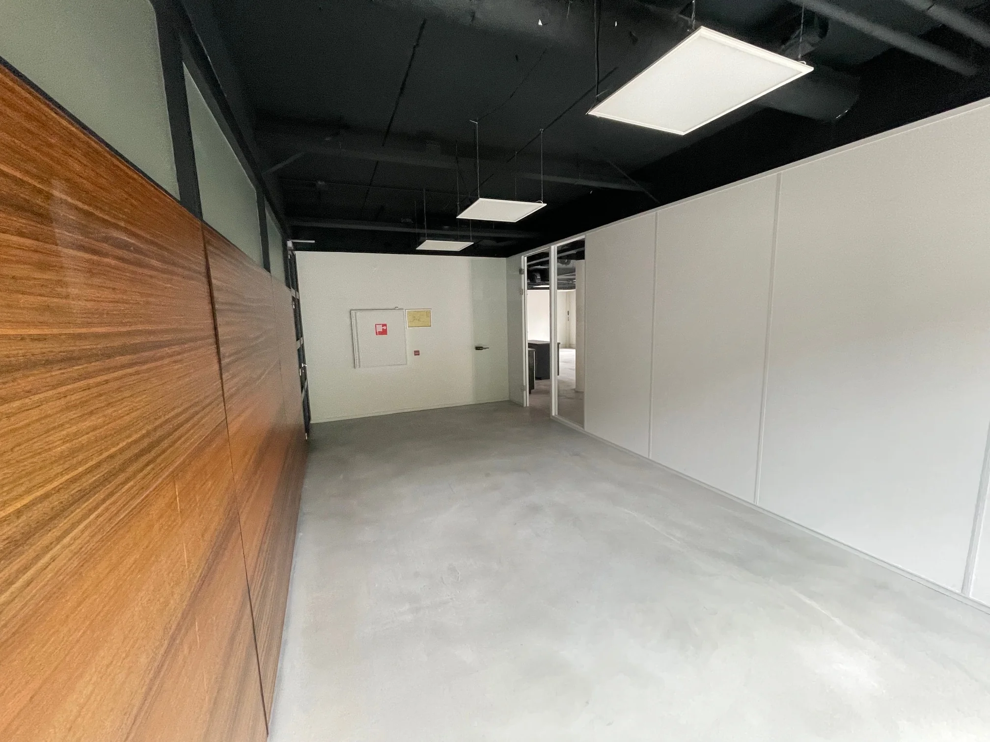Gang in een modern kantoorgebouw met strakke witte wanden, een houten wandpaneel en een betonnen vloer.