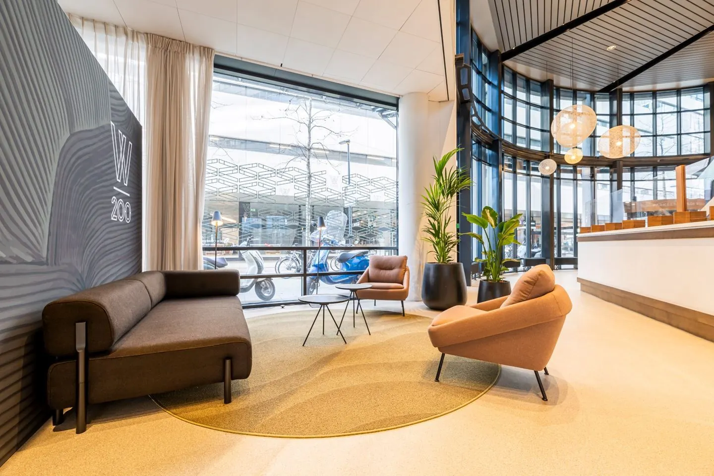 Een moderne lobby met comfortabele zitgelegenheid, grote ramen en planten.
