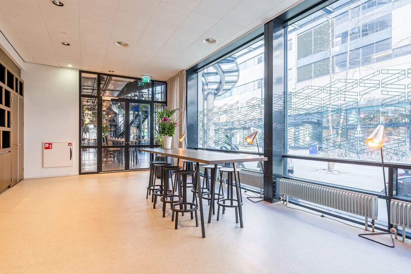 Een moderne kantoorruimte met een lange tafel, barkrukken en grote ramen die uitzicht bieden op de straat.