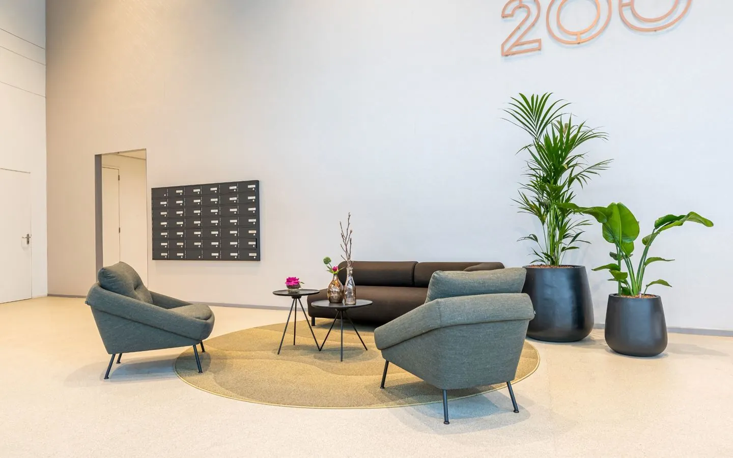 Een moderne wachtruimte met comfortabele stoelen, planten en een grote wanddecoratie met het nummer 200.