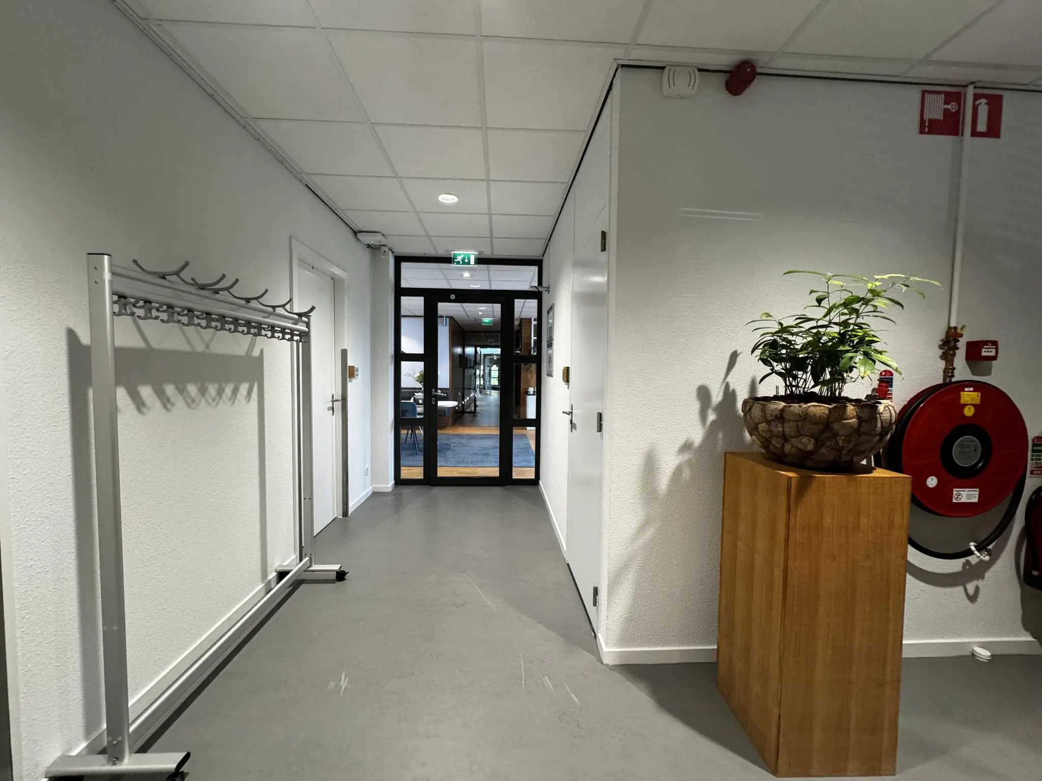 Hal met kapstok, plant in stenen bloempot op houten sokkel en brandslanghaspel in een kantoorgebouw aan de Softwareweg.