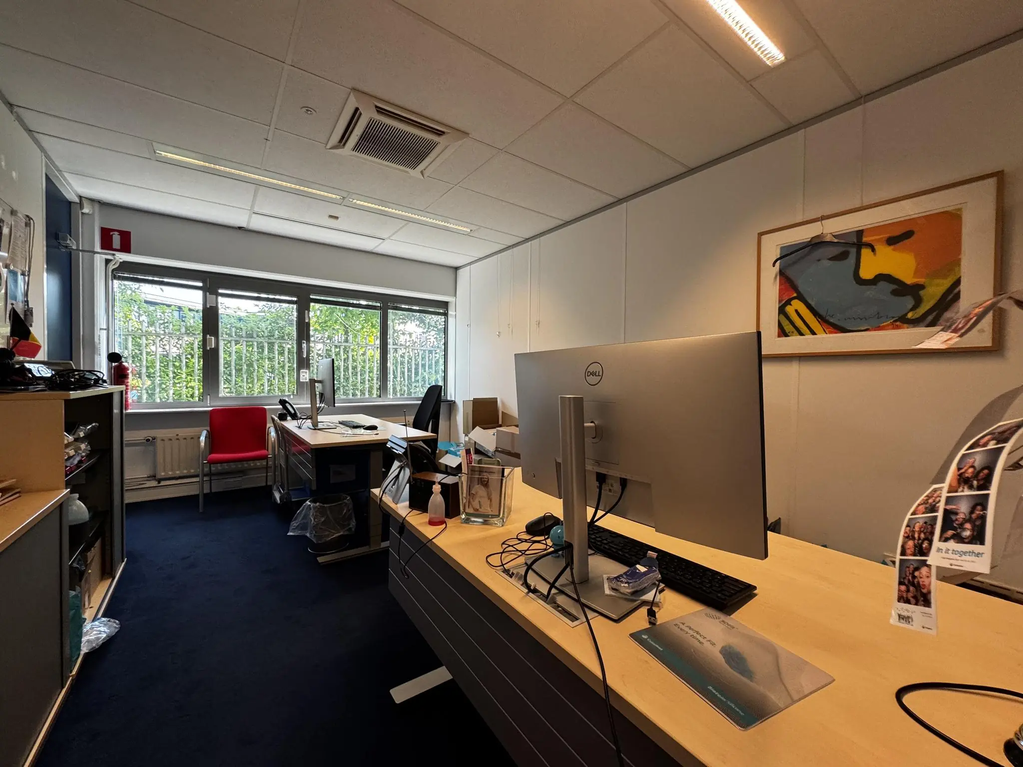 Modern kantoor met twee bureaus, computers en een groot raam met uitzicht op groen.